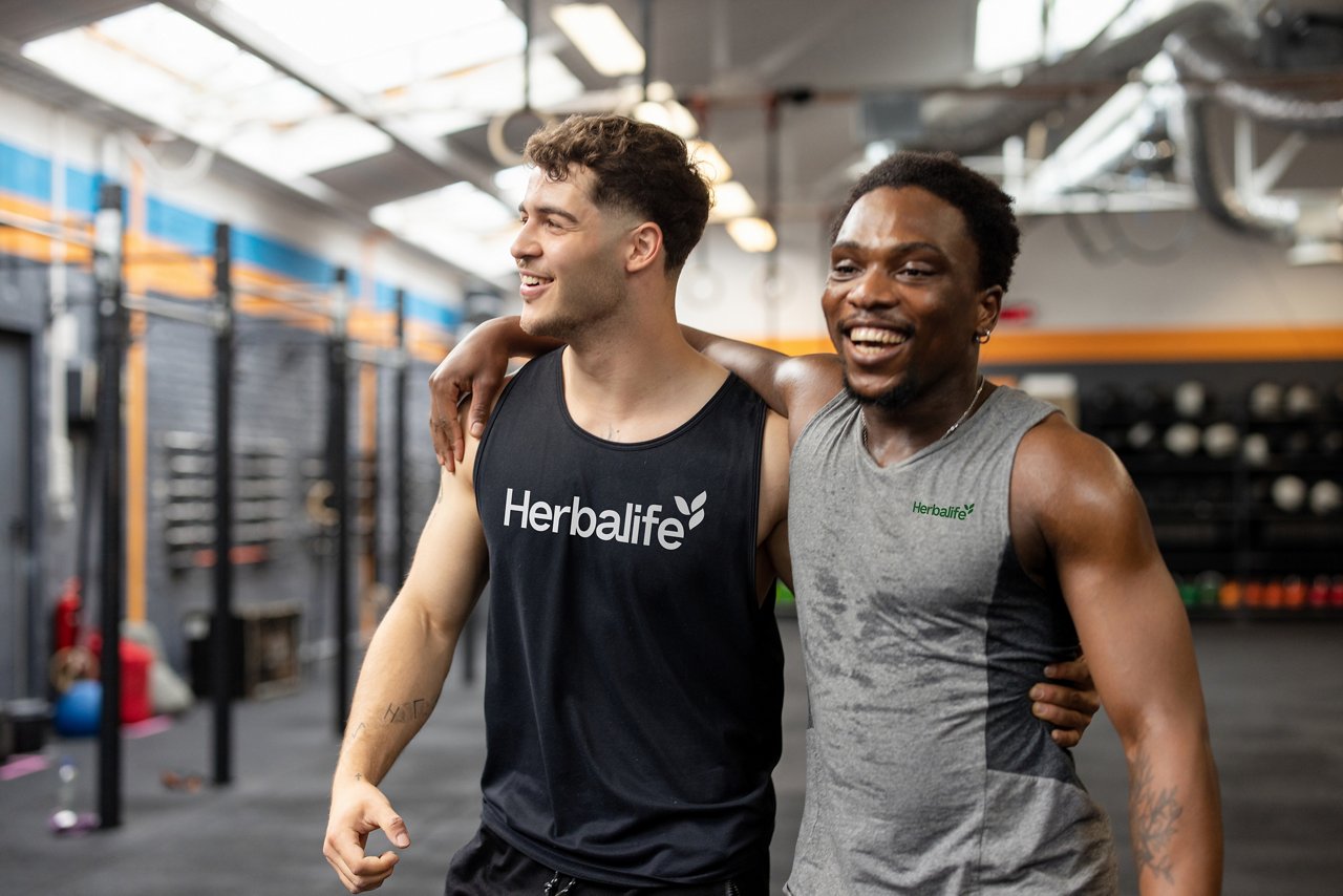 Friends Supporting Each Other at the Gym Two men at the gym laughing, one arm around the other, wearing herbalife workout clothes