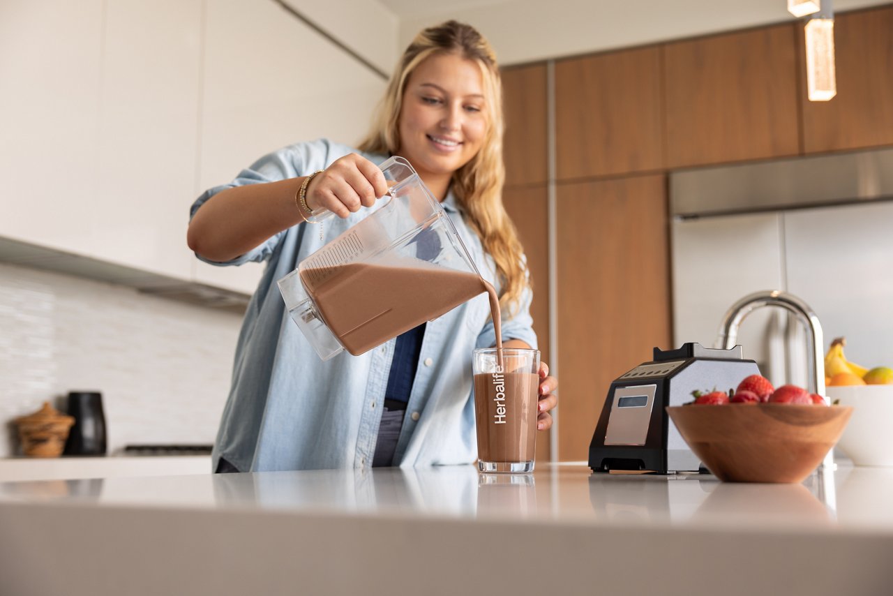 Woman smiles before enjoying a chocolate shake in her home.