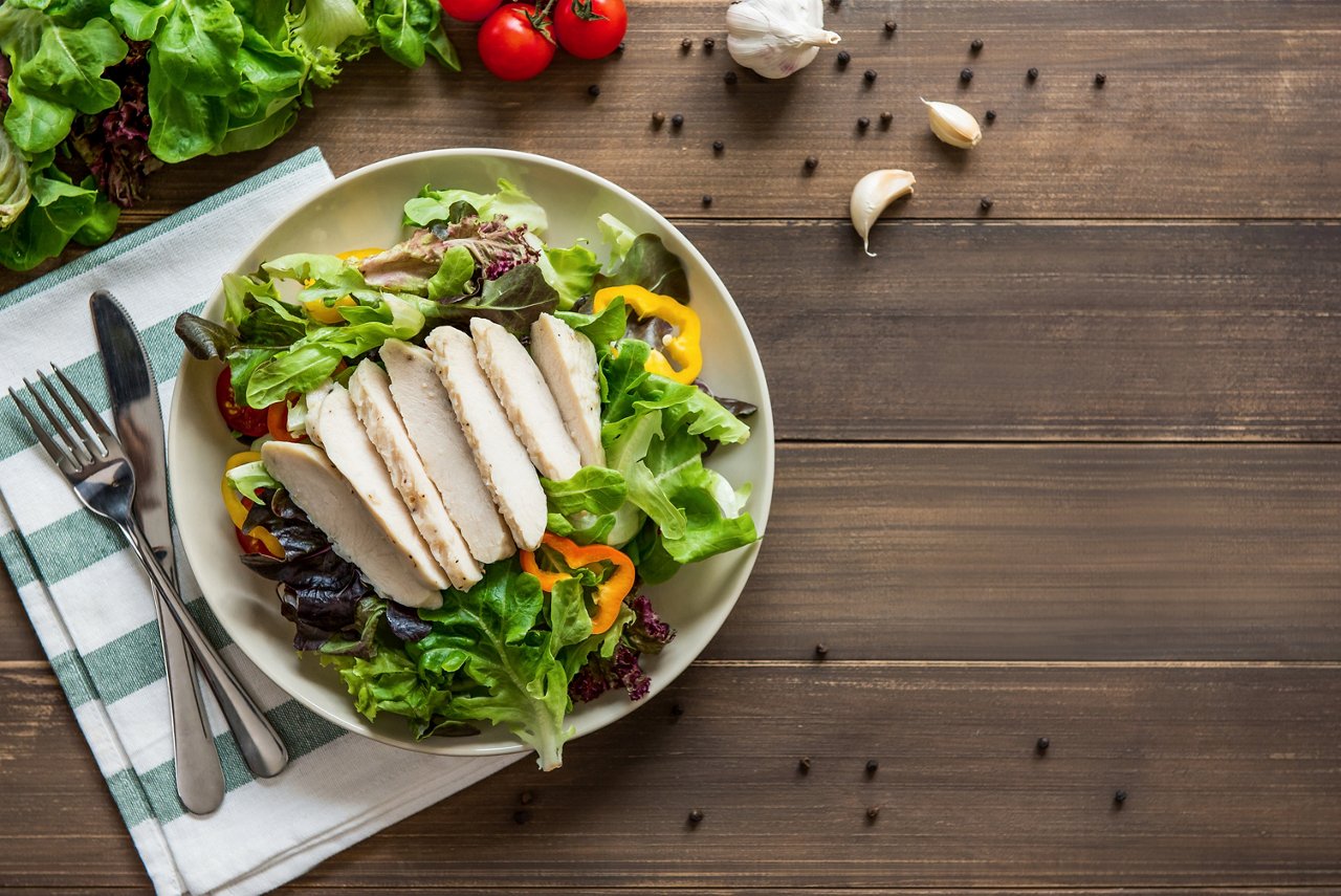 Chicken with salad on a plate with cutlery Healthy food, ready to eat mix fresh vegetable salad with skinless boiled chicken breast, top view on wood table background with copy space