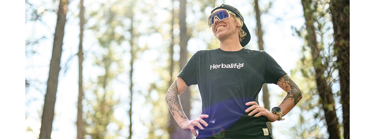 ​​​​Heather Jackson, elite endurance athlete and Herbalife-sponsored runner, stands outdoors in running gear and hydration vest, looking focused before a trail run. 