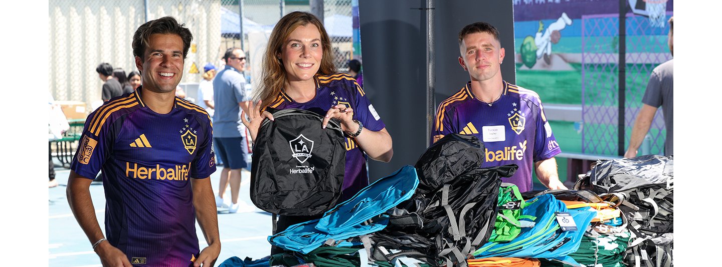 LA Galaxy midfielder Riqui Puig, Herbalife vice president of regional sales and business development Samantha Holway, and forward Tucker Lepley help distribute backpacks to kids and families at the annual Back-to-School event in South Los Angeles.