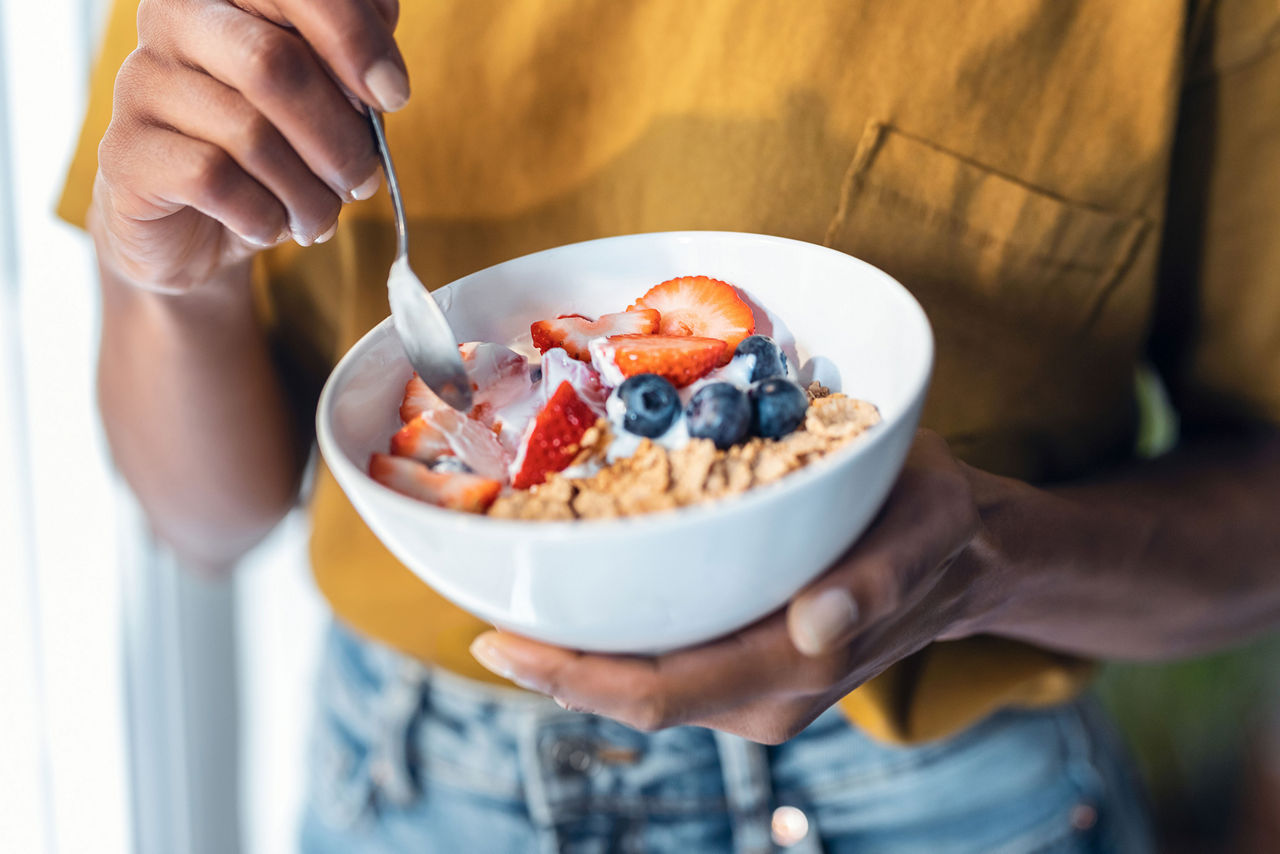 Mujer sosteniendo un plato de yogur con muesli y fruta